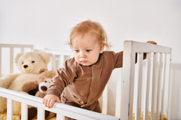 happy childhood, adorable toddler boy standing in crib with soft toys in cozy nursery room at home