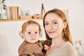 happy mother with adorable toddle son in hands looking at camera in nursery room at home, motherhood