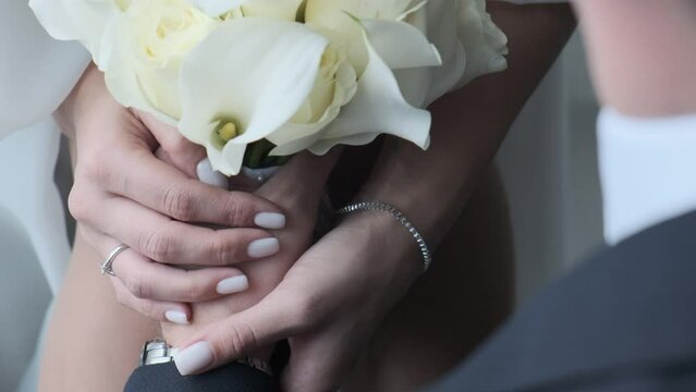 A bride in a gorgeous white chalet holds a bridal bouquet of white calla lilies. A close-up shot of her hand arranging the flowers.