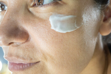 Skincare portrait. A young woman spread hydration cream on her face. Close up portrait of female...