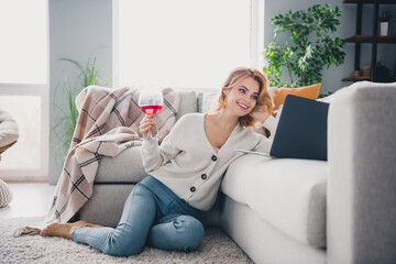 Full size portrait of cheerful pretty girl sit barefoot comfy carpet hold wine glass use laptop enjoy pastime flat indoors