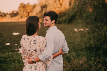 Obraz premium Happy, smiling couple in a green park with the sunset light, hugging, kissing, walking hand in hand, and lying on the ground and grass, representing their love outdoors and sincere love