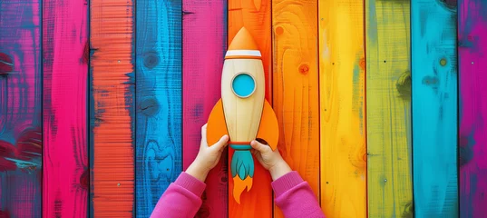 Fototapeten Launch of a red rocket on colorful wooden background, made of wood, held by children's hands. Successful start concept. © Igor Link