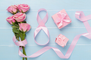 Composition with pink roses, gift box and eight made of ribbon on wooden background, top view. Women's day concept