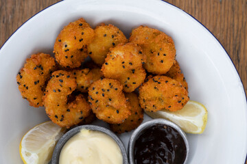Seafood. Top view of a white bowl with fried panko shrimps with lemon, aioli and teriyaki dipping sauces, on the wooden table.	