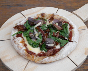Food. Closeup view of a homemade crusty pizza with mozzarella cheese, arugula, cured ham and red onion.