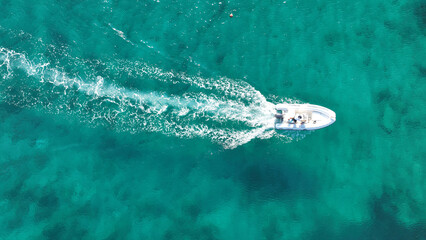 Aerial drone top down photo of small inflatable rib speed boat cruising in high speed deep emerald sea of Mykonos island, Cyclades, Greece