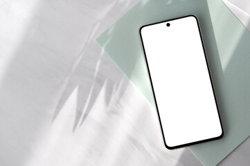 Smartphone with empty screen mockup on pastel sage green paper and neutral gray marble desk background with aesthetic floral natural sun light shadows, elegant spring business branding template