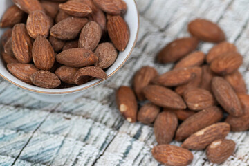 Close up roasted organic brown almond seed on wooden table and some of almond in white decorative porcelain cup