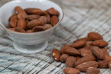 Close up roasted organic brown almond seed on wooden table and some of almond in white decorative porcelain cup