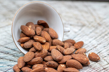 Close up roasted organic brown almond seed on wooden table and some of almond in white porcelain cup