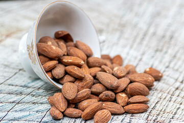 Close up roasted organic brown almond seed on wooden table and some of almond in white decorative porcelain cup