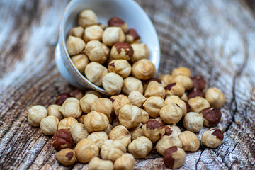 Peeled and roasted organically grown hazelnuts spilling out of a ceramic bowl on wooden table, close-up of healthy roasted hazelnuts, healthy snacks