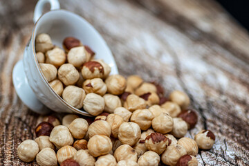 Peeled and roasted organically grown hazelnuts spilling out of a ceramic bowl on wooden table, close-up of healthy roasted hazelnuts, healthy snacks