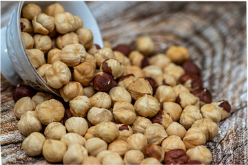 Peeled and roasted organically grown hazelnuts spilling out of a ceramic bowl on wooden table, close-up of healthy roasted hazelnuts, healthy snacks