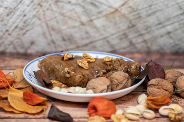 Turkish Baklava sweet cake on the plate, decorated with fresh pistachios, nuts, vanilla and dry autumn leaves, on wooden massive table  