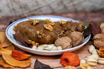 Turkish Baklava sweet cake on the plate, decorated with fresh pistachios, nuts, vanilla and dry autumn leaves, on wooden massive table  