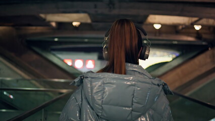 Woman walking dark subway in headphones listening music close up back view 