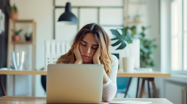 A girl suffering from spring vitamin deficiency sits tired and sleepy at her laptop.