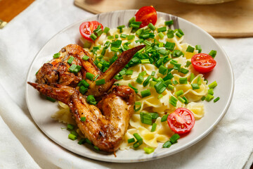 Farfalle pasta with grilled chicken wings garnished with cherry tomatoes and green onions