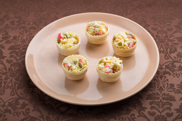 Salad in tartlets on a beige plate on a brown tablecloth