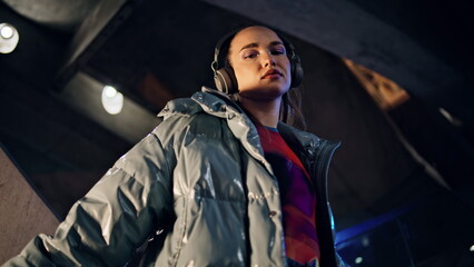 Confident woman posing headphones at dark urban backdrop close up. Woman relax 