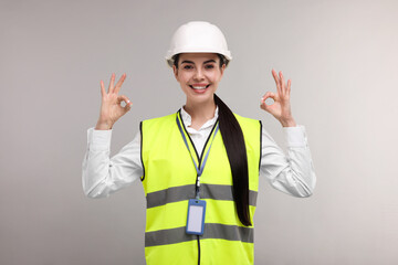 Engineer with hard hat and badge showing ok gesture on grey background