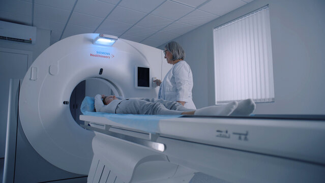 Professional radiologist lays female patient in MRI or CT or PET scan machine. Doctor conducts check up procedure in clinic with advanced medical technologies. High-tech modern medical equipment.