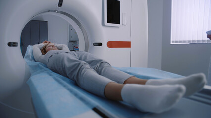 Close up shot of woman lying on CT or PET or MRI scan bed and moving inside machine. Scanning of...