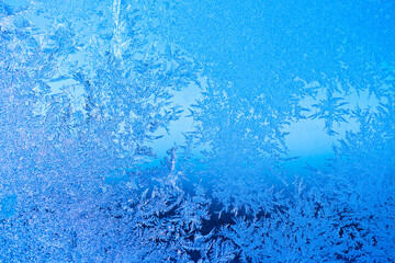 Frost patterns on a window in winter day (blue background)