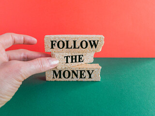 Follow the money symbol. Concept words Follow the money on beautiful brick blocks. Beautiful green table red background. Businessman hand. Business and follow the money concept. Copy space.