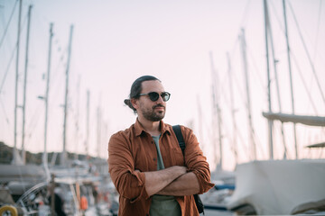 A young, stylish man in sunglasses at the marina among the sea yachts.