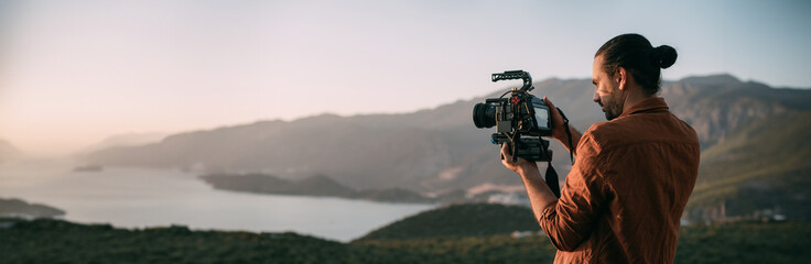A young Caucasian man with a professional camera in his hands on a mountain by the sea.