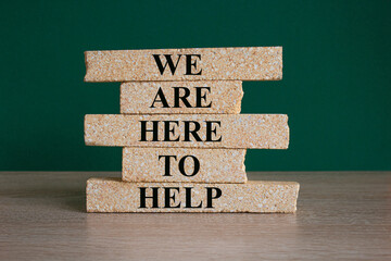 We are here to help symbol. Concept words we are here to help on brick blocks. Beautiful green...