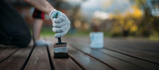 Close-up, a man's hand in a work glove with a painting brush paints boards outdoors.