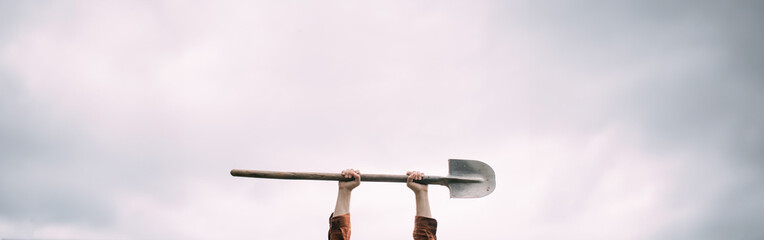 A man's hand holds a bayonet shovel on a white background. Metal shovel in his hands against the sky
