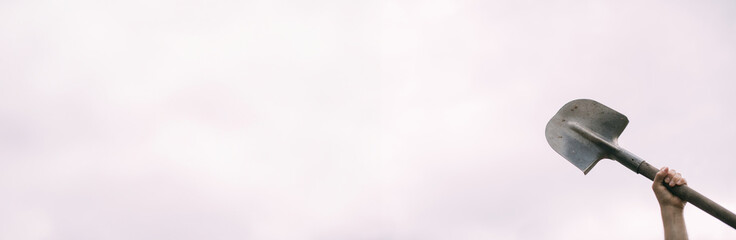A man's hand holds a bayonet shovel on a white background. Metal shovel in his hands against the sky