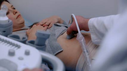 Caucasian woman lies undergoing ultrasound diagnostics in modern clinic or hospital. Medical specialist, doctor does check up of abdominal organs to female patient using advanced sonography equipment.