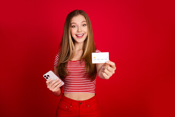 Photo of excited sweet girl wear striped top enjoying online banking modern device showing you credit card isolated red color background