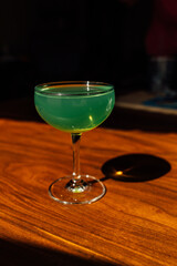 green absinthe drink in cocktail coupe glass on wooden table in the sun