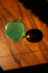 green absinthe drink in a coupe glass with on wooden table in the sun with shadow