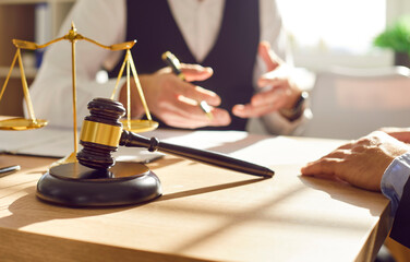 Close up of judge's gavel and scales of justice on table in law firm office. Judge's wooden gavel on background of lawyer who advises client. Legal consultation and law services concept. 