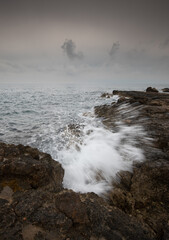 Windy waves splashing with power on a rocky coast in winter. Stormy weather outdoor