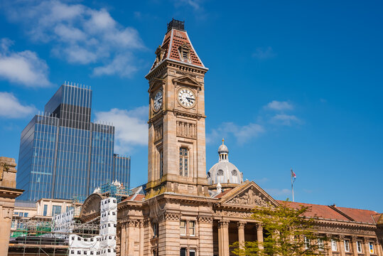 Historical building with a clock tower in Birmingham, UK, contrasts with modern structures under a clear sky, showcasing the city's architectural evolution.