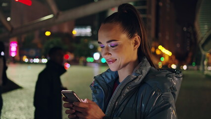 Happy girl reading message phone at night street closeup. Lady scrolling content