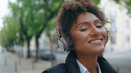 African girl listening music by headphones on street close up. Woman enjoy sound