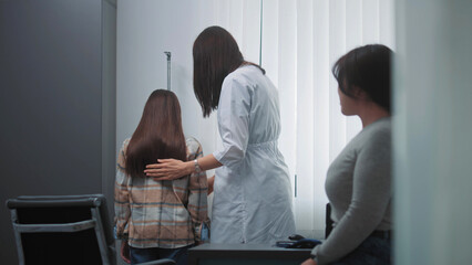 Female doctor, endocrinologist weighs and measures height of Asian girl in hospital office. Young...