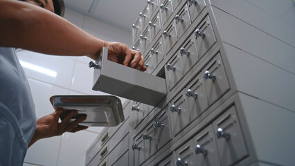 Asian nurse puts samples with blood tests or histology biological tissues analysis in medical metal storage cabinet with racks. Female scientist, microbiologist works in modern scientific laboratory.