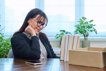 Middle-aged joyful woman with new books unpacked from cardboard box