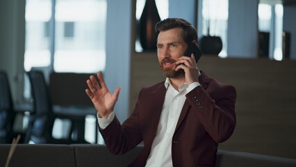 Cheerful businessman talking mobile phone in big office interior. Happy discuss